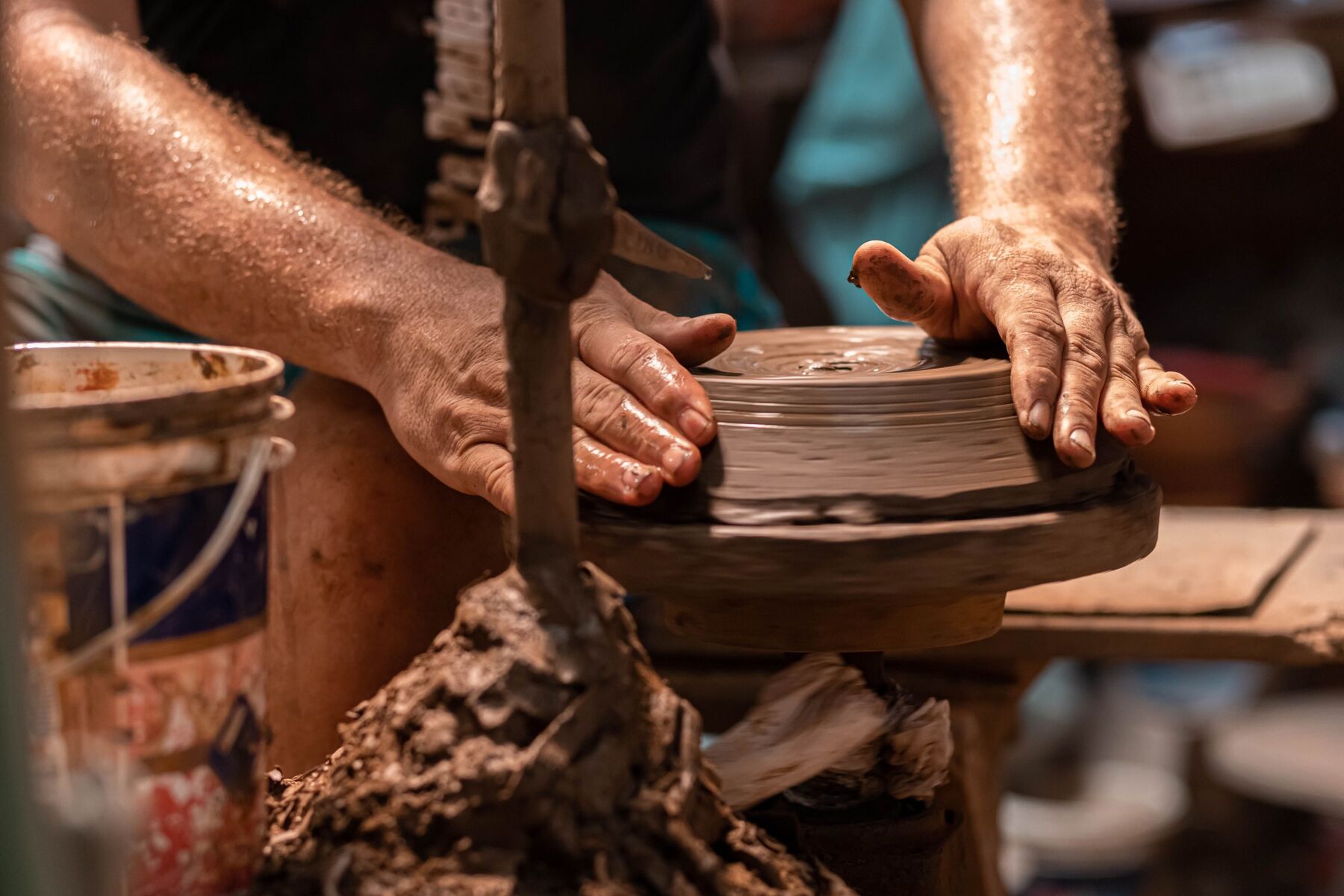 Mãos sujas de barro moldando uma peça no torno