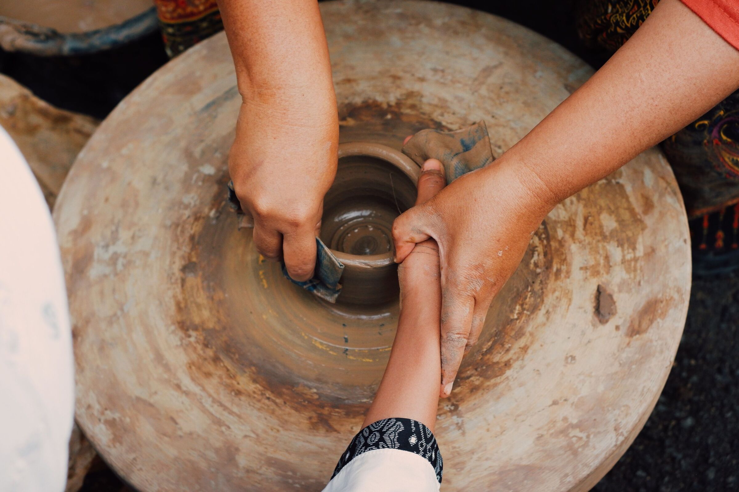 Mãos de um adulto guiando as mãos de uma criança no torno de barro
