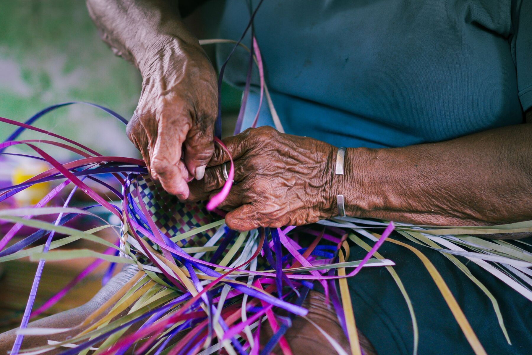 Mãos de uma senhora trançando fitas de palha coloridas