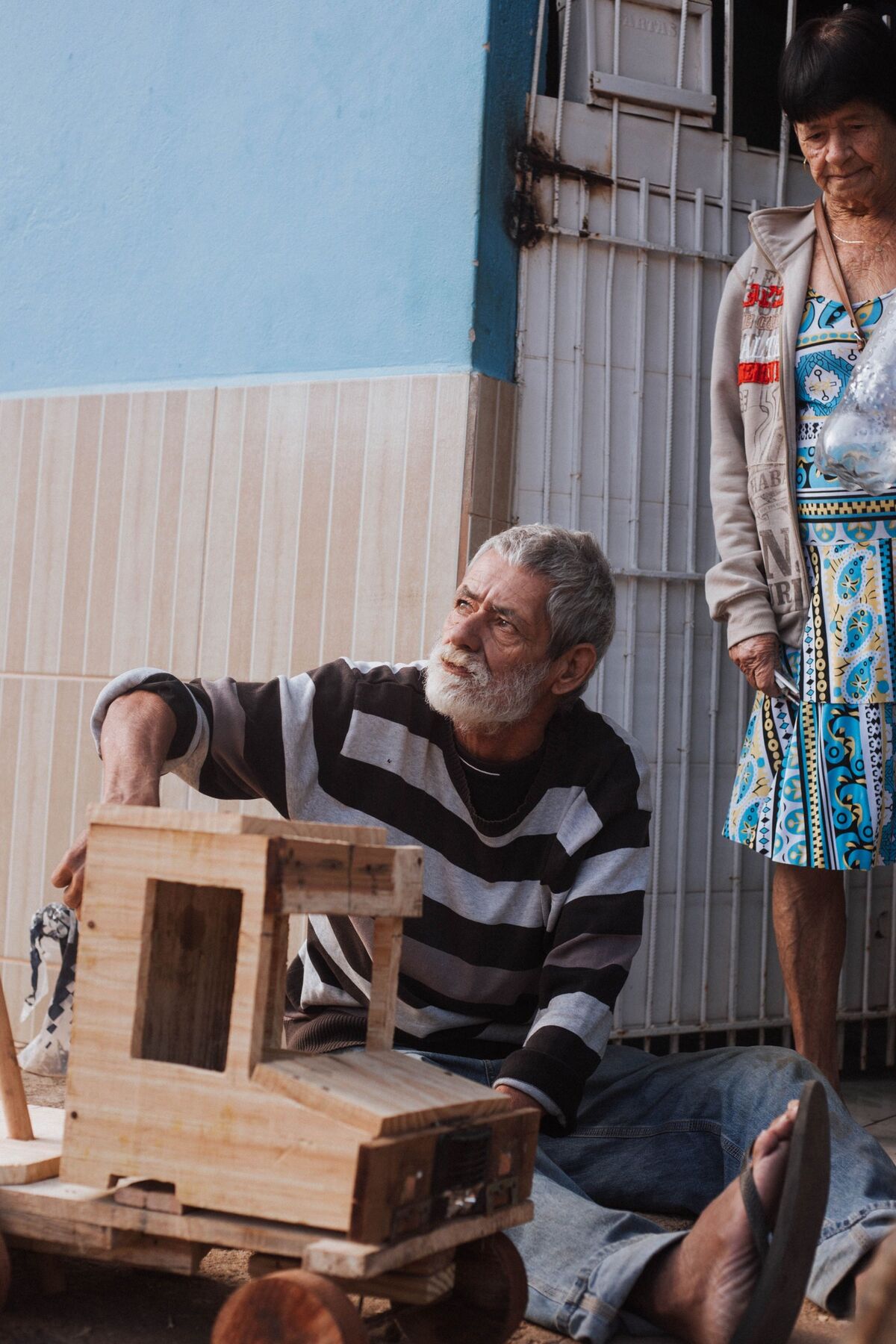 Senhor de barba branca sentado no chão ao lado de um caminhão de madeira